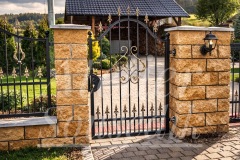 Kovaná vstupní branka s ozdobnými hroty mezi kamennými sloupky